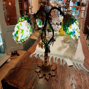 Lámpara de sobremesa vintage realizada con motivos agrícolas al ser sus tulipas tres racimos de uva fabricados a mano en vidrio de Murano y la viña en cobre recreando sus retorcidas formas y hojas típicas de parra.
